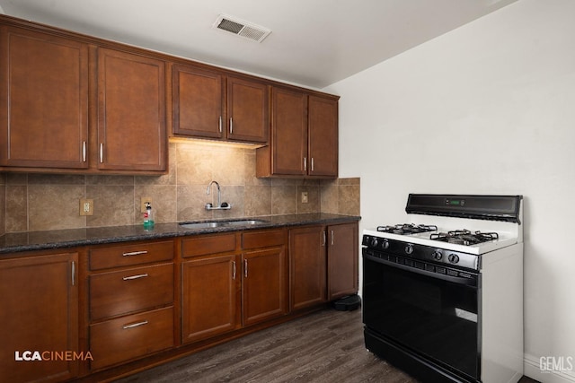 kitchen with range with gas cooktop, a sink, dark wood finished floors, dark stone countertops, and backsplash