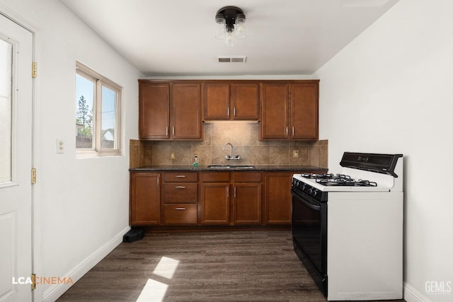 kitchen featuring gas range oven, a sink, dark wood-style floors, brown cabinets, and backsplash
