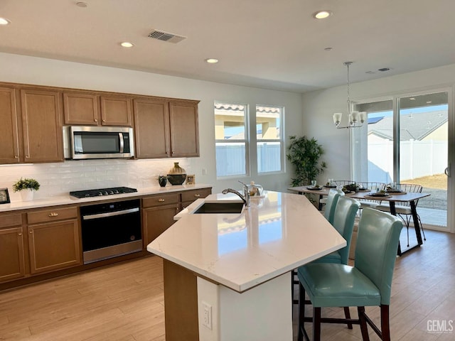 kitchen with pendant lighting, sink, stainless steel appliances, an island with sink, and a chandelier