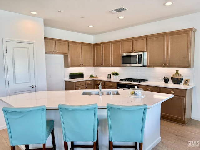 kitchen featuring stainless steel appliances, sink, an island with sink, and light hardwood / wood-style flooring