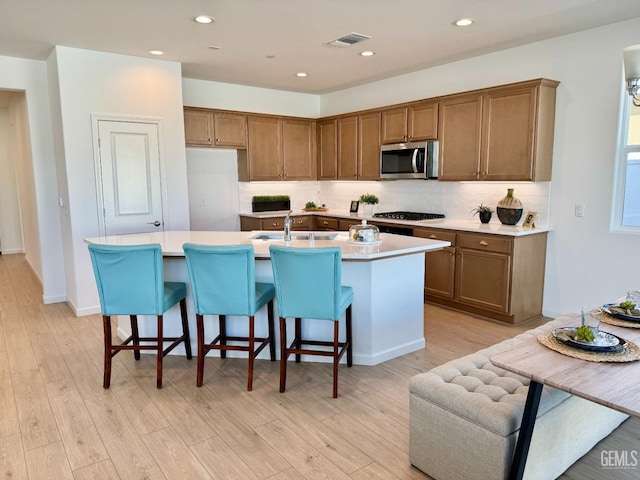 kitchen featuring a kitchen island with sink, backsplash, a breakfast bar area, and light hardwood / wood-style floors