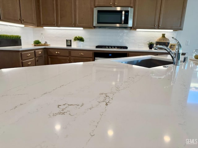 kitchen with light stone counters, sink, backsplash, and gas cooktop