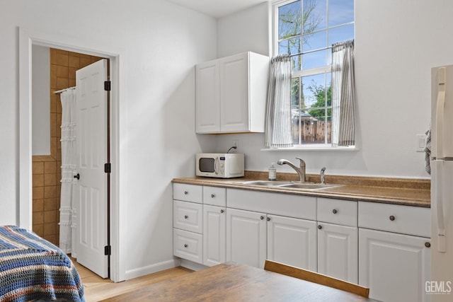 kitchen featuring white appliances, a sink, white cabinets, light wood-style floors, and dark countertops