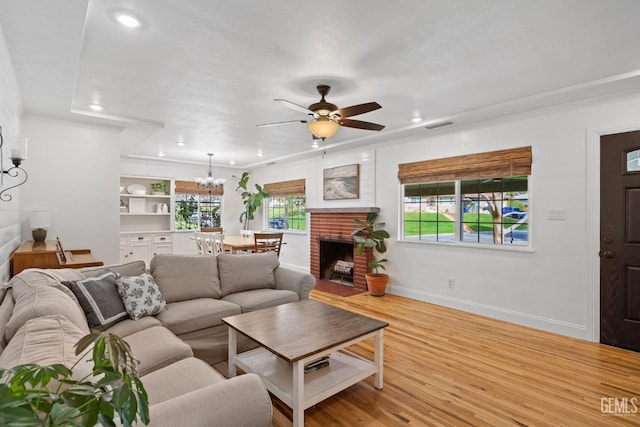 living area with visible vents, light wood-style flooring, ornamental molding, ceiling fan with notable chandelier, and baseboards