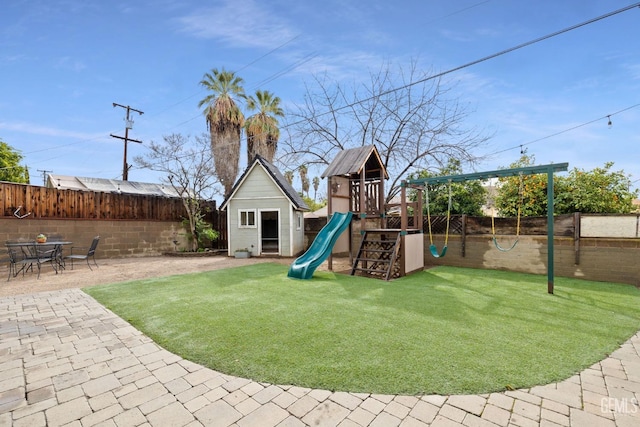 view of playground featuring a patio area, a yard, a fenced backyard, and an outbuilding