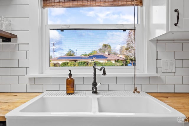 interior details with white cabinets, backsplash, wooden counters, and a sink