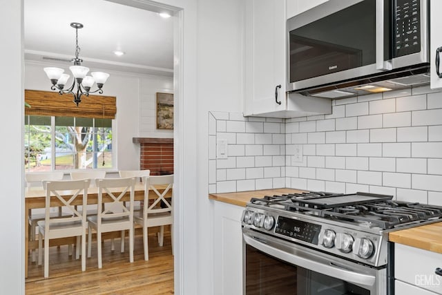 kitchen with ornamental molding, white cabinetry, appliances with stainless steel finishes, wooden counters, and a chandelier