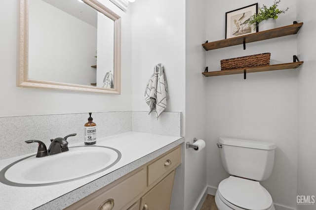 half bathroom featuring baseboards, toilet, and vanity