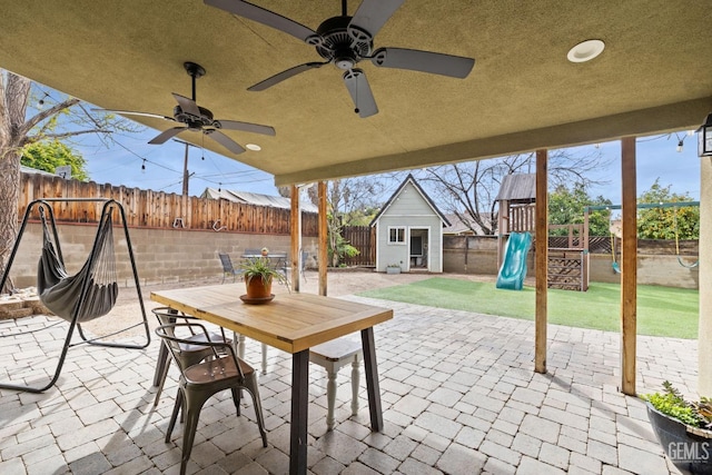 view of patio / terrace featuring a playground, a shed, an outdoor structure, a fenced backyard, and outdoor dining space