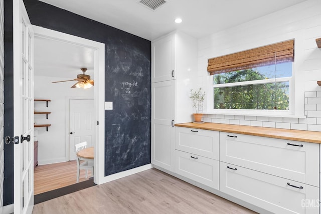 kitchen with visible vents, light wood-style flooring, butcher block countertops, decorative backsplash, and white cabinetry