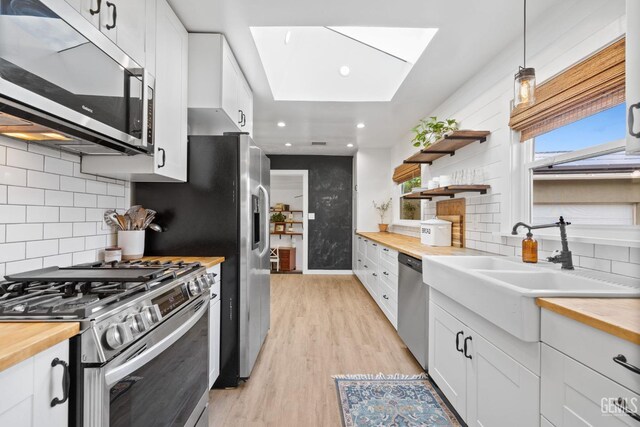 kitchen with a skylight, light wood finished floors, butcher block counters, and stainless steel appliances