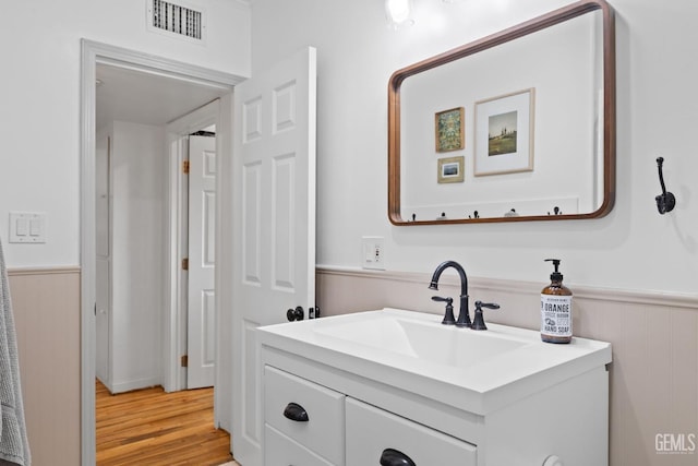 bathroom with a wainscoted wall, visible vents, wood finished floors, and vanity