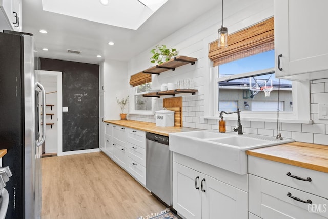 kitchen featuring wooden counters, light wood-style floors, appliances with stainless steel finishes, tasteful backsplash, and a wealth of natural light