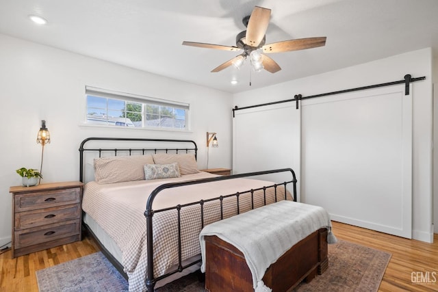 bedroom with a ceiling fan, a barn door, recessed lighting, and light wood-type flooring