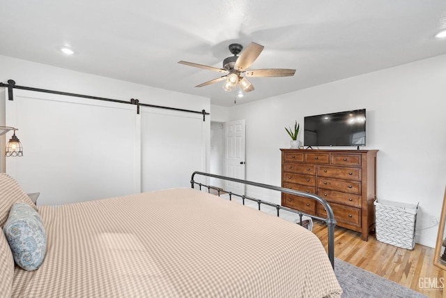 bedroom featuring recessed lighting, ceiling fan, a barn door, and wood finished floors