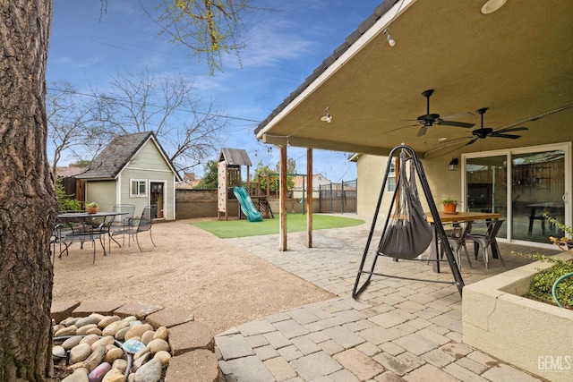 view of patio / terrace with an outbuilding, a playground, outdoor dining area, and fence