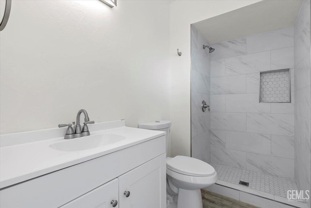 bathroom with tiled shower, hardwood / wood-style floors, vanity, and toilet