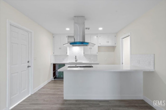 kitchen with kitchen peninsula, island range hood, sink, white cabinets, and light hardwood / wood-style floors