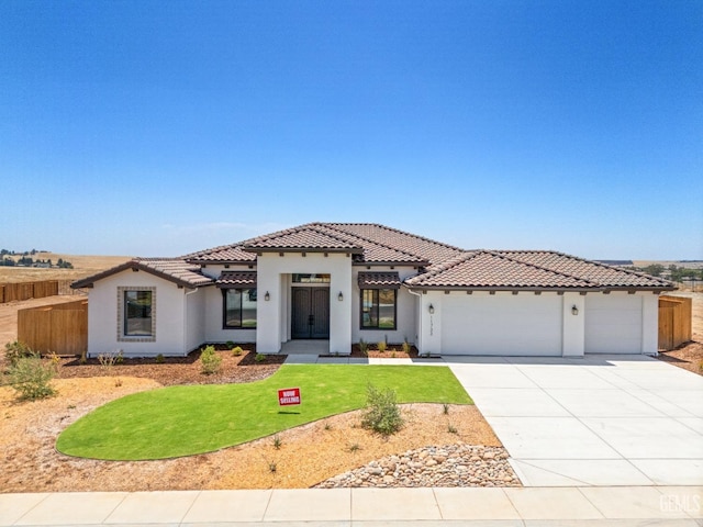 mediterranean / spanish-style house with stucco siding, driveway, a tile roof, a front yard, and an attached garage