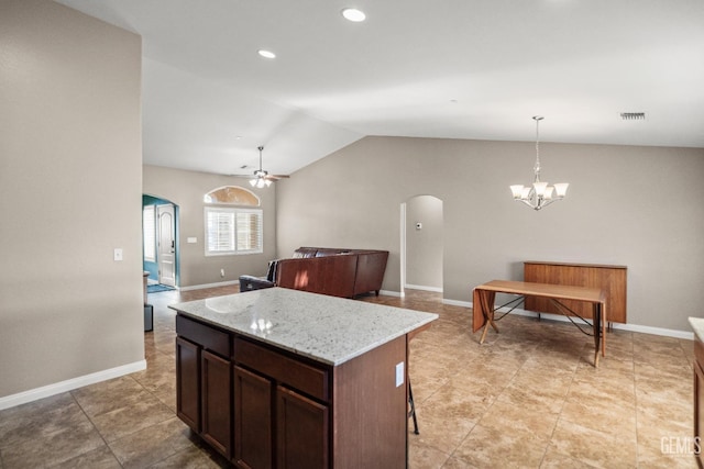 kitchen with a center island, ceiling fan with notable chandelier, vaulted ceiling, light stone countertops, and decorative light fixtures