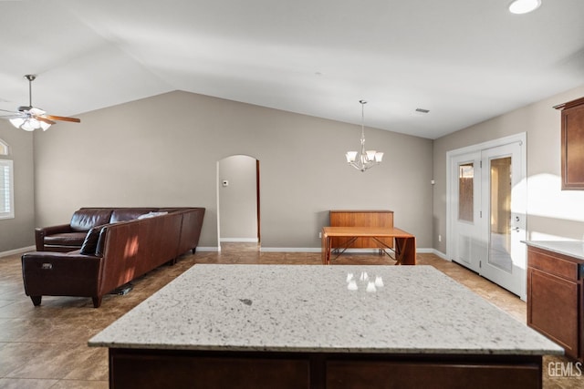 kitchen with pendant lighting, lofted ceiling, ceiling fan with notable chandelier, a kitchen island, and light stone counters