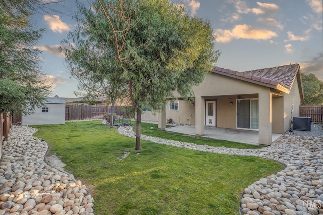 back house at dusk with a lawn, central AC, a patio, and a storage shed