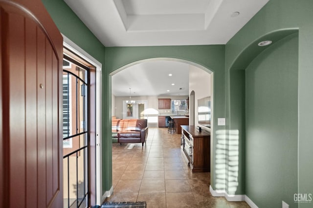 entrance foyer with a raised ceiling, light tile patterned floors, and an inviting chandelier