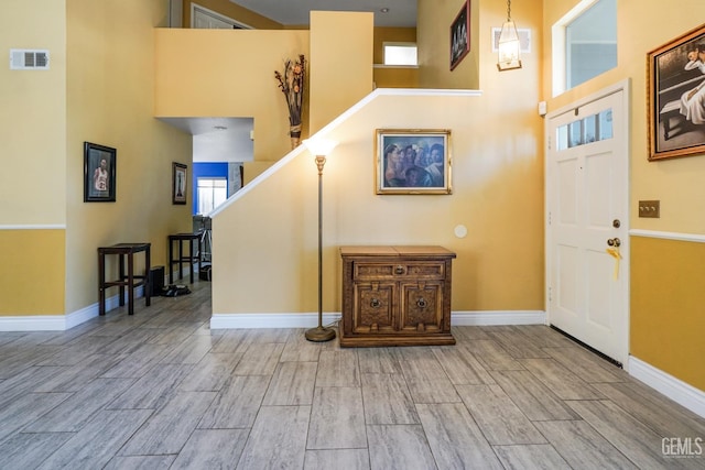 foyer entrance with wood finish floors, visible vents, stairway, a high ceiling, and baseboards