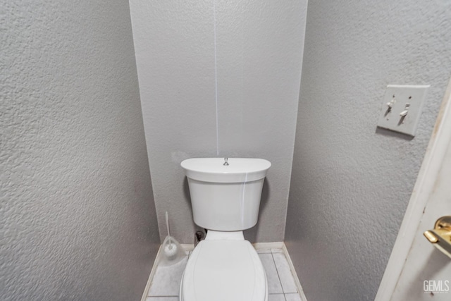 bathroom with toilet, tile patterned floors, and a textured wall