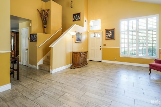 foyer featuring high vaulted ceiling, baseboards, visible vents, and stairway