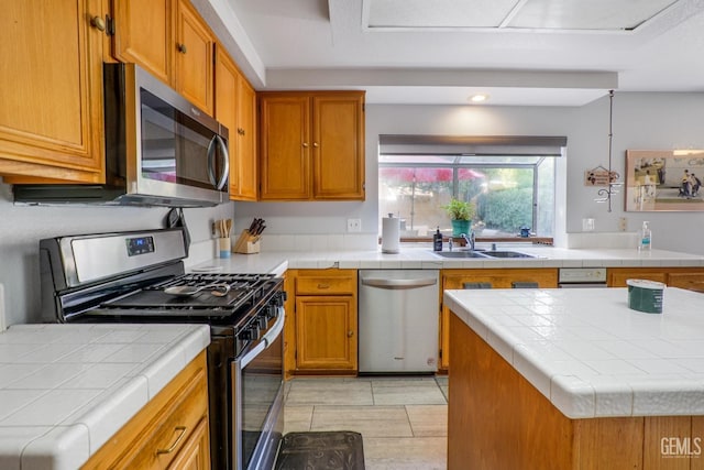 kitchen with tile countertops, brown cabinetry, stainless steel appliances, and a sink