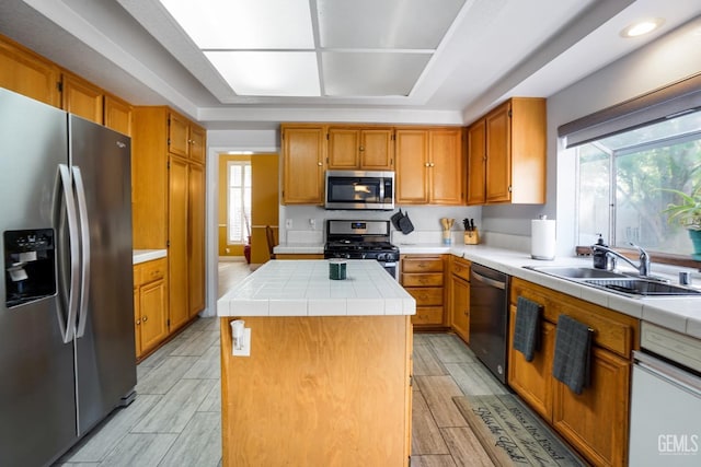 kitchen featuring wood finish floors, stainless steel appliances, tile counters, a kitchen island, and a sink