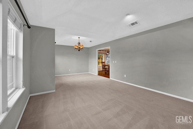 carpeted spare room with a textured ceiling and an inviting chandelier