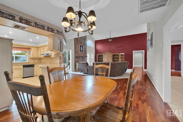 dining area with a large fireplace, ceiling fan with notable chandelier, hardwood / wood-style flooring, and high vaulted ceiling