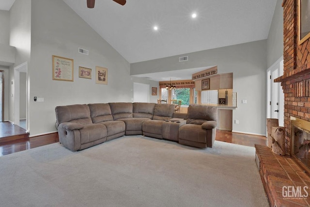 living room with high vaulted ceiling, light carpet, a brick fireplace, and ceiling fan with notable chandelier