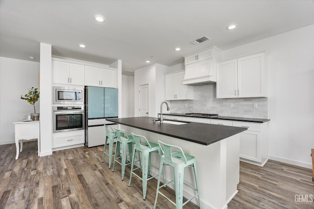 kitchen with dark countertops, a sink, dark wood finished floors, appliances with stainless steel finishes, and visible vents