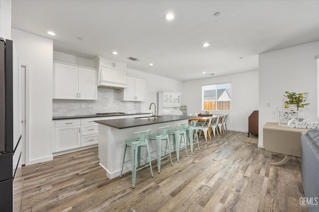 kitchen featuring custom range hood, dark countertops, a breakfast bar area, and light wood-style flooring
