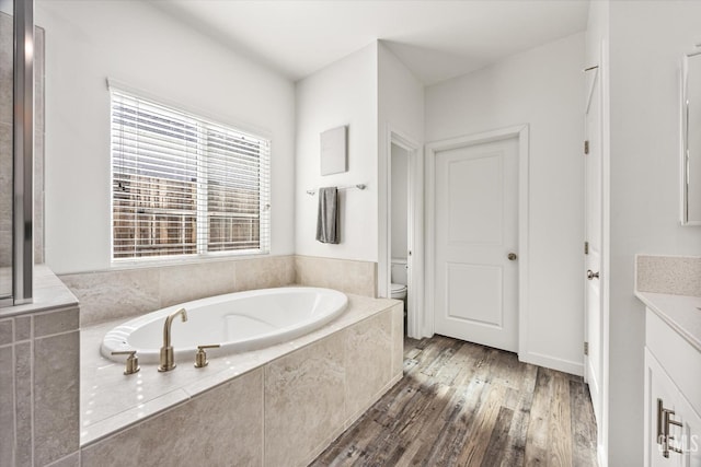 full bath with a bath, toilet, vanity, and wood finished floors