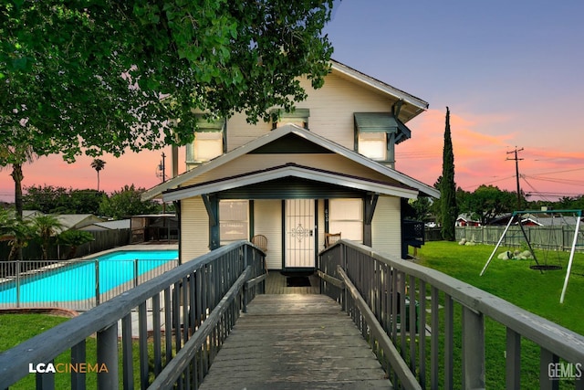 back house at dusk with a lawn, a fenced in pool, and a playground