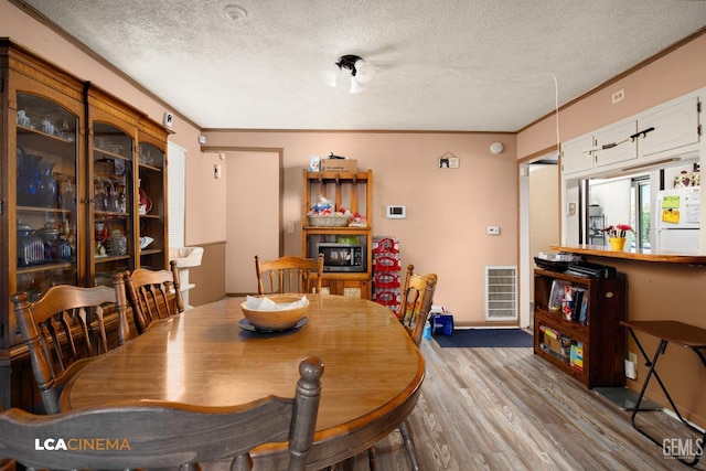 dining space with a textured ceiling, light wood-type flooring, and crown molding