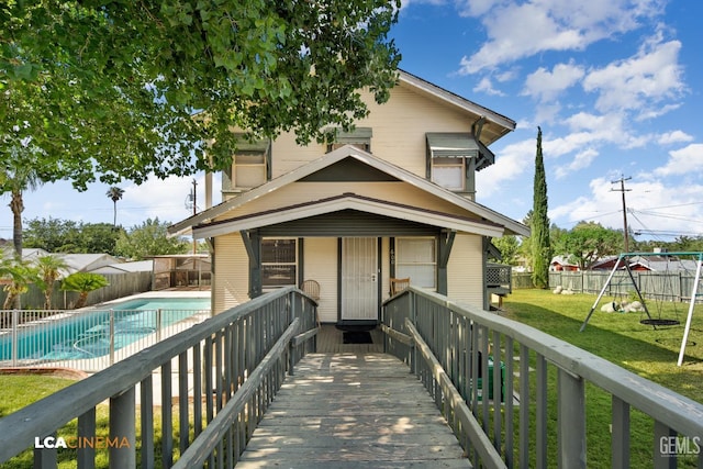 rear view of house featuring a playground, a yard, and a fenced in pool