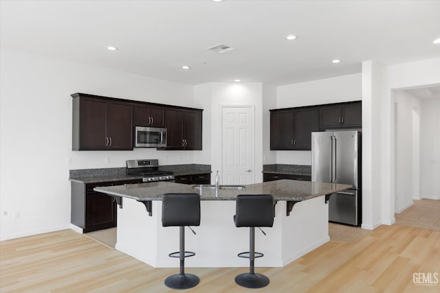 9702 Petersburg Pl, Bakersfield, CA 93306 - kitchen with appliances with stainless steel finishes, a sink, a breakfast bar, light wood-type flooring, and a kitchen island with sink