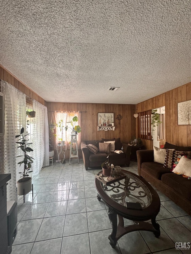living room featuring a textured ceiling, visible vents, wood walls, and light tile patterned floors