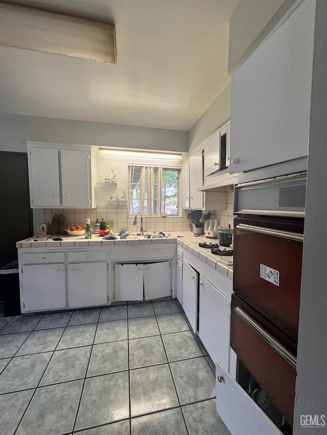 kitchen featuring tile counters, white cabinets, light tile patterned floors, a warming drawer, and backsplash