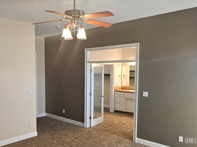 unfurnished bedroom with a walk in closet, carpet, baseboards, and ceiling fan