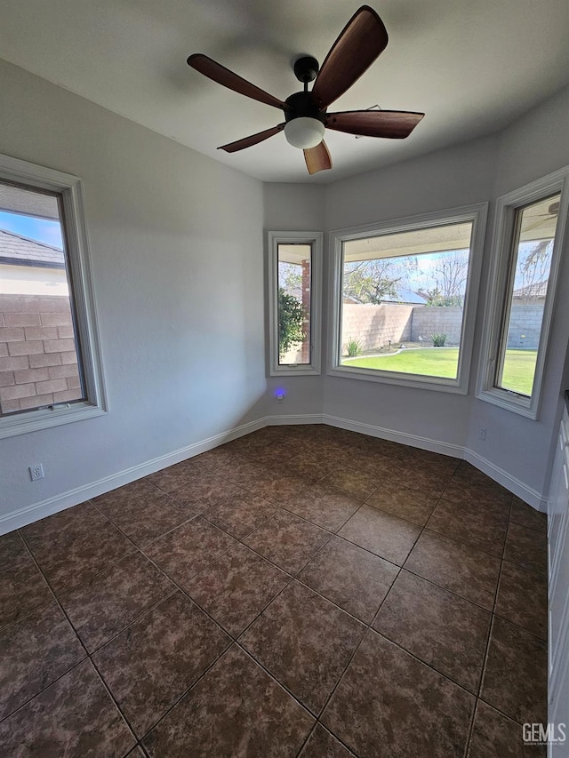 spare room featuring a ceiling fan, baseboards, and dark tile patterned flooring