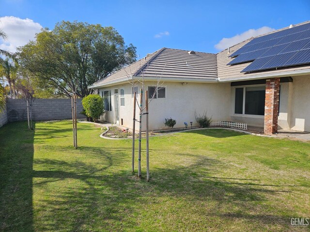 back of property featuring roof mounted solar panels, a fenced backyard, stucco siding, a tile roof, and a lawn
