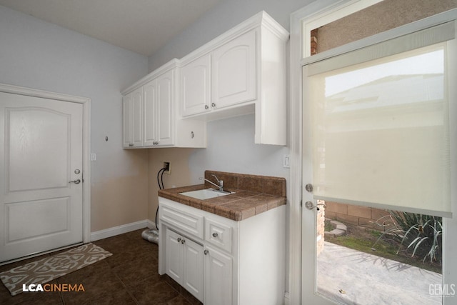 laundry room featuring a sink, baseboards, hookup for a washing machine, cabinet space, and dark tile patterned flooring