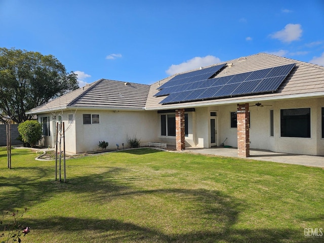 rear view of house featuring a tile roof, a patio area, roof mounted solar panels, a yard, and stucco siding