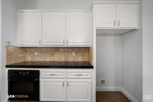 kitchen with dark countertops, decorative backsplash, baseboards, white cabinetry, and black oven